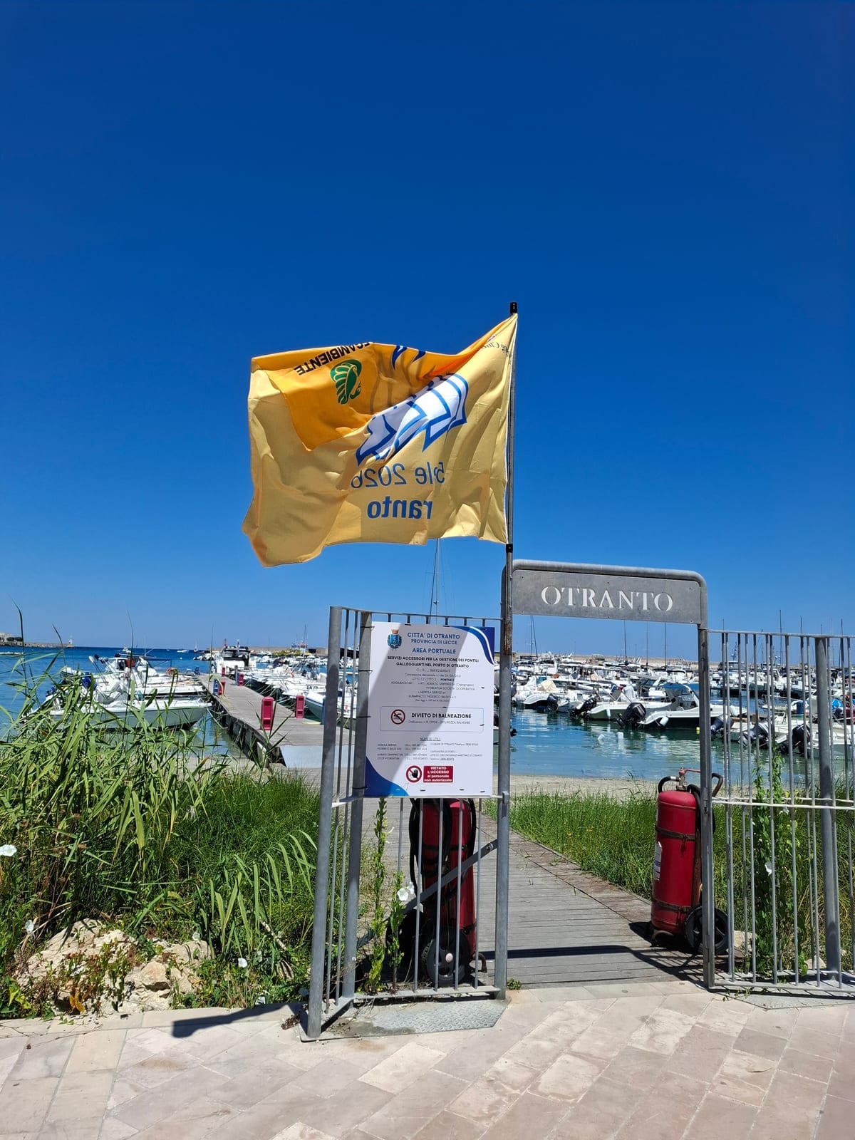 Ingresso del pontile al porto di Otranto: cancello con insegna OTRANTO e bandiera gialla